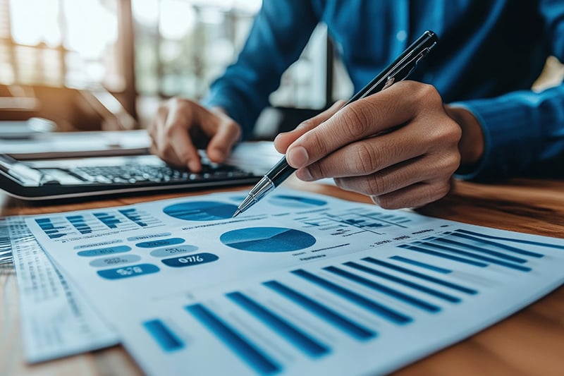 person pointing to printed charts and graphs on desk